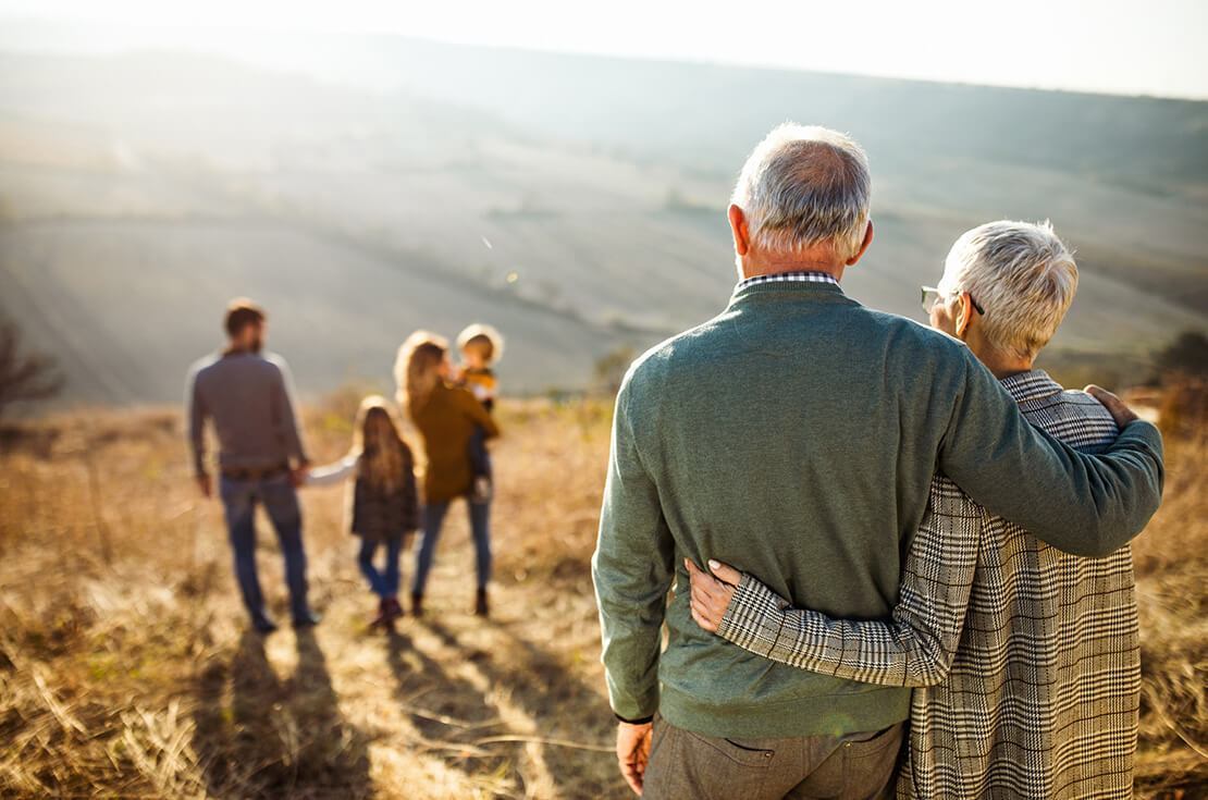 Back view of embraced grandparents enjoying while looking at their family on a field in autumn day